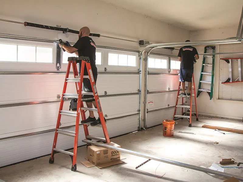 Two technicians on ladders installing a garage door opener