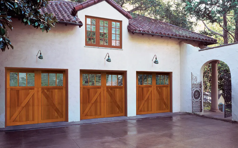 Three wood carriage-style garage doors on a white stucco home