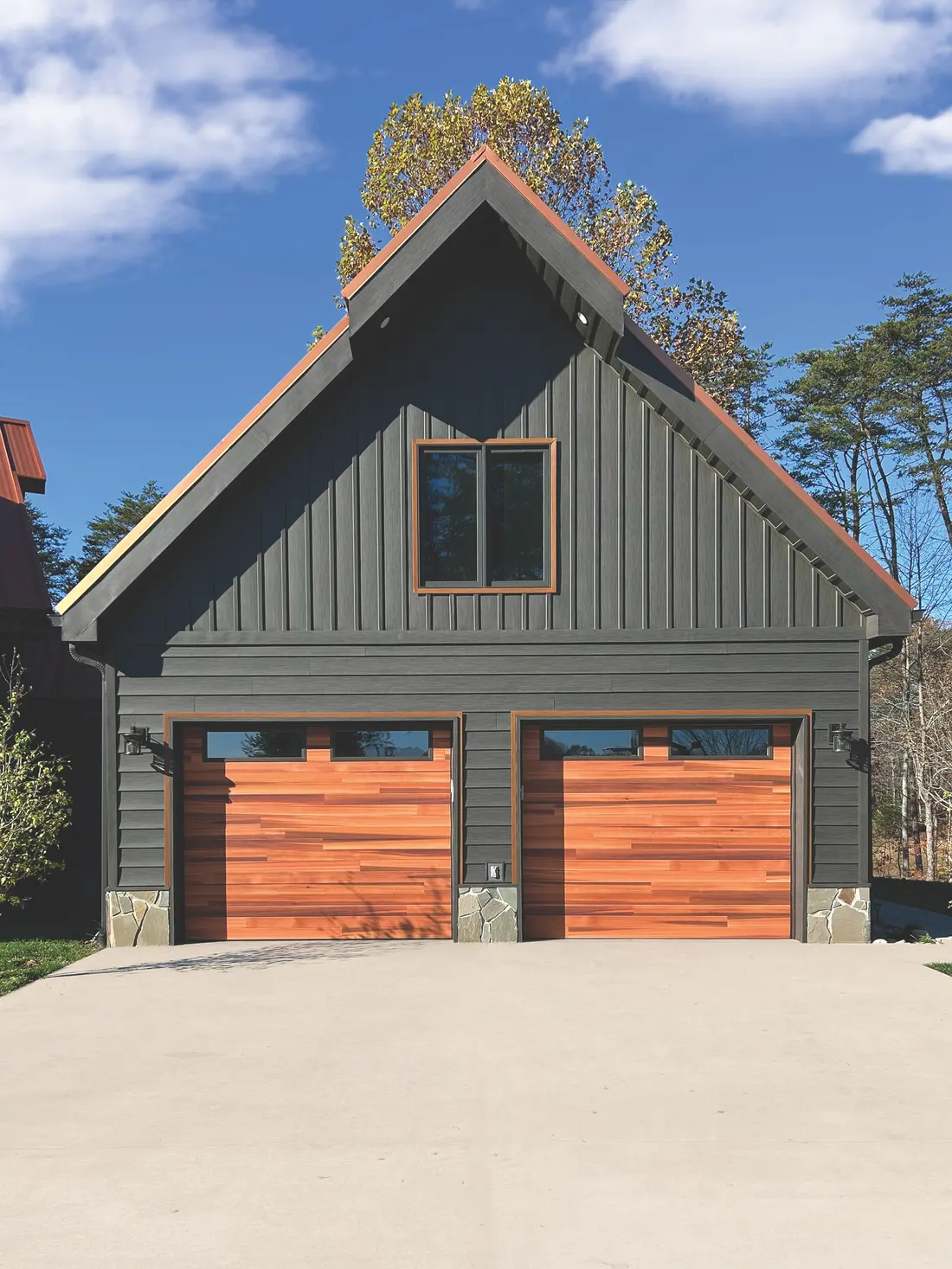 A dark green home with two cedar plank garage doors